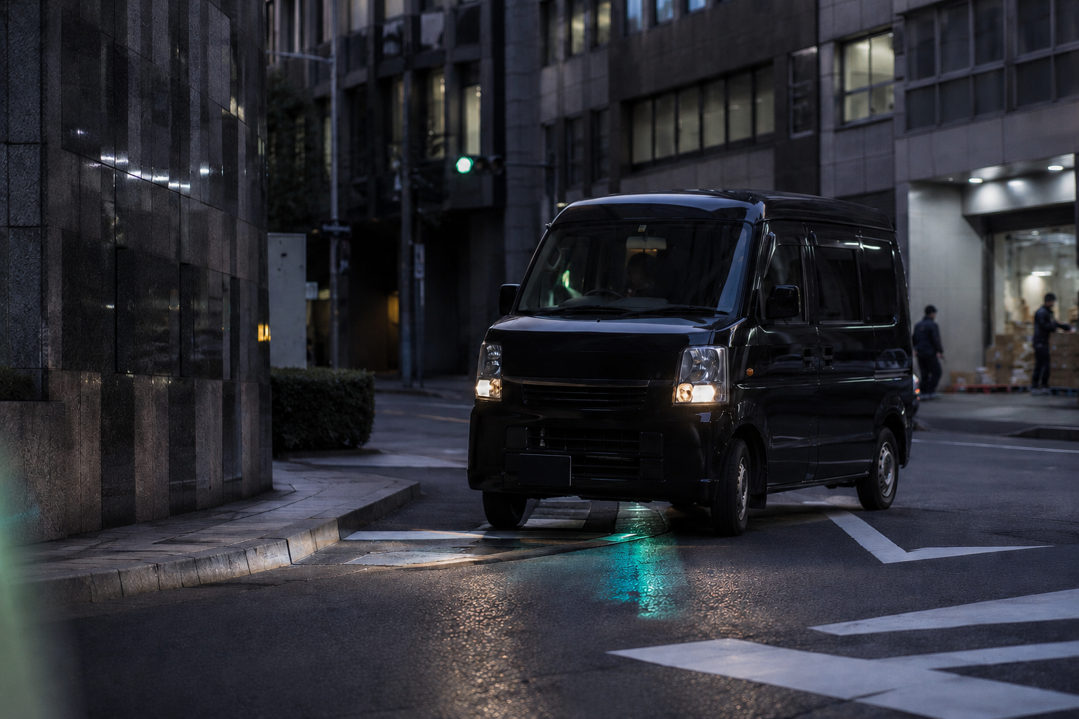 夜のオフィス街の交差点で停車する黒い軽貨物車両